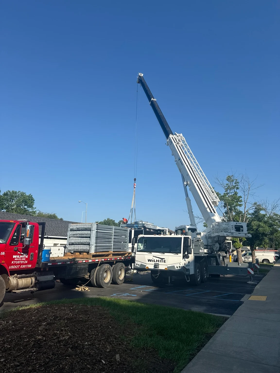 Mobile crane with extended boom and lifting rigging beside a flatbed carrying large cooling-system components